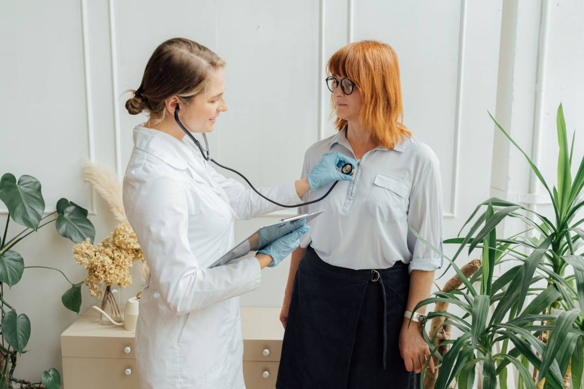 A clinician in a white coat taking a seated patient’s blood pressure