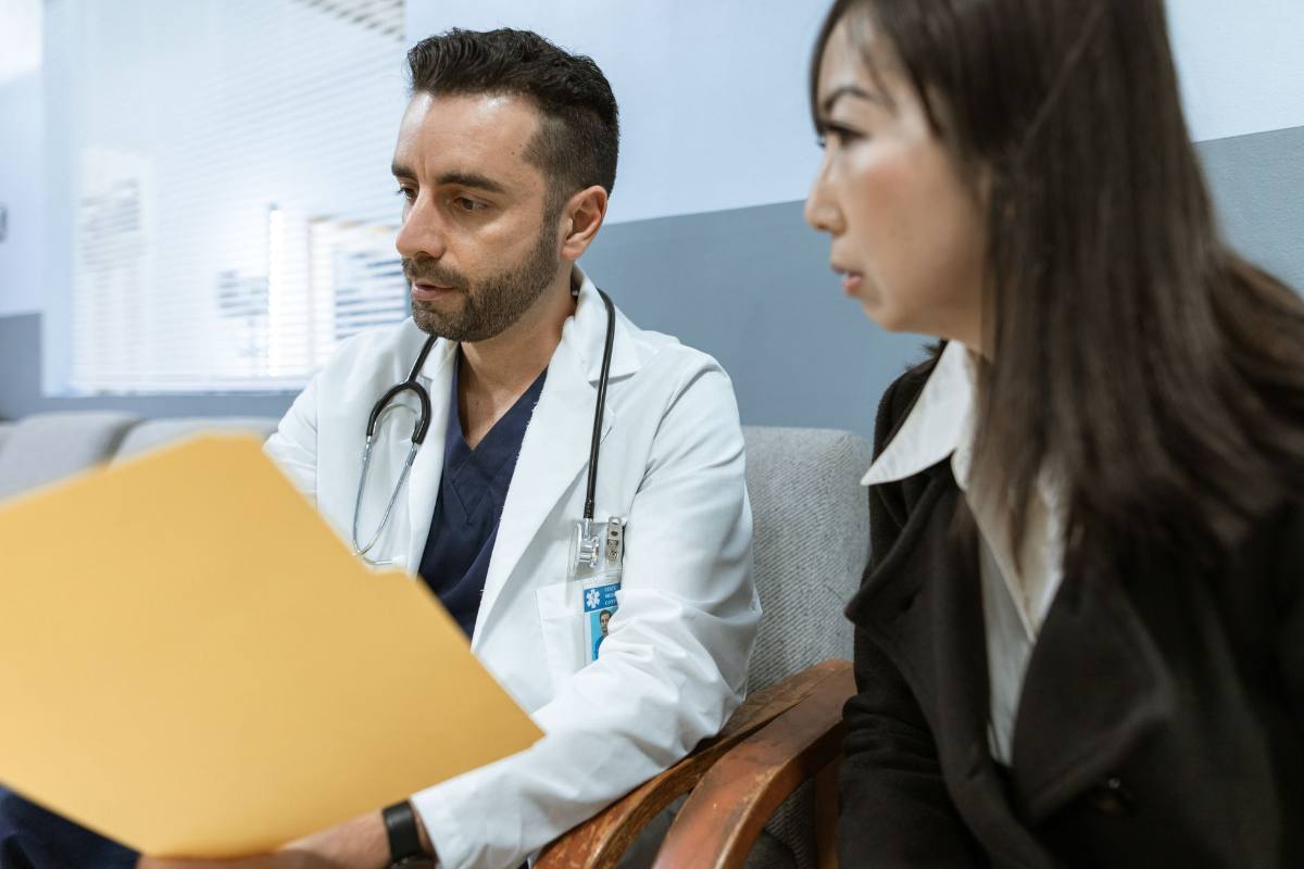 A clinician holding an open case file, talking with a patient seated beside them