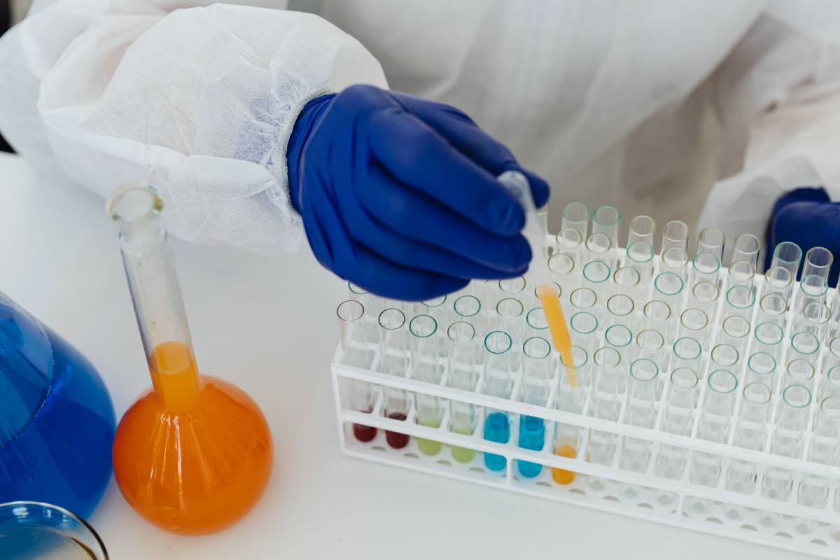 A gloved researcher using a pipette to fill a rack of test tubes holding colored liquid