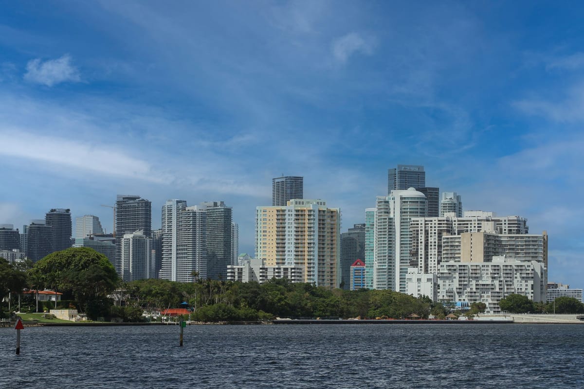 A line of white and pastel high-rise towers along a bay, seen from the water with a green shoreline in front of them