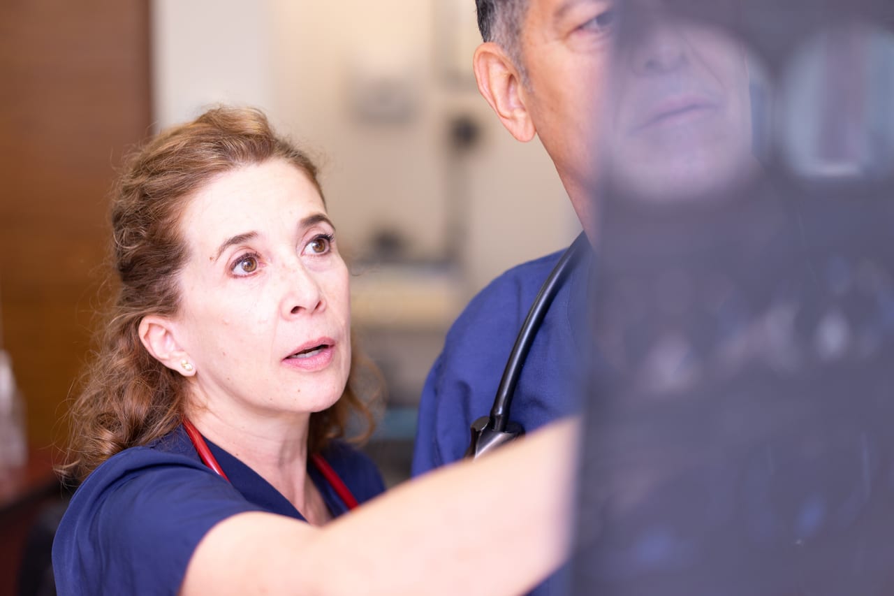 A nurse in navy scrubs with a red stethoscope reading an imaging film beside a colleague