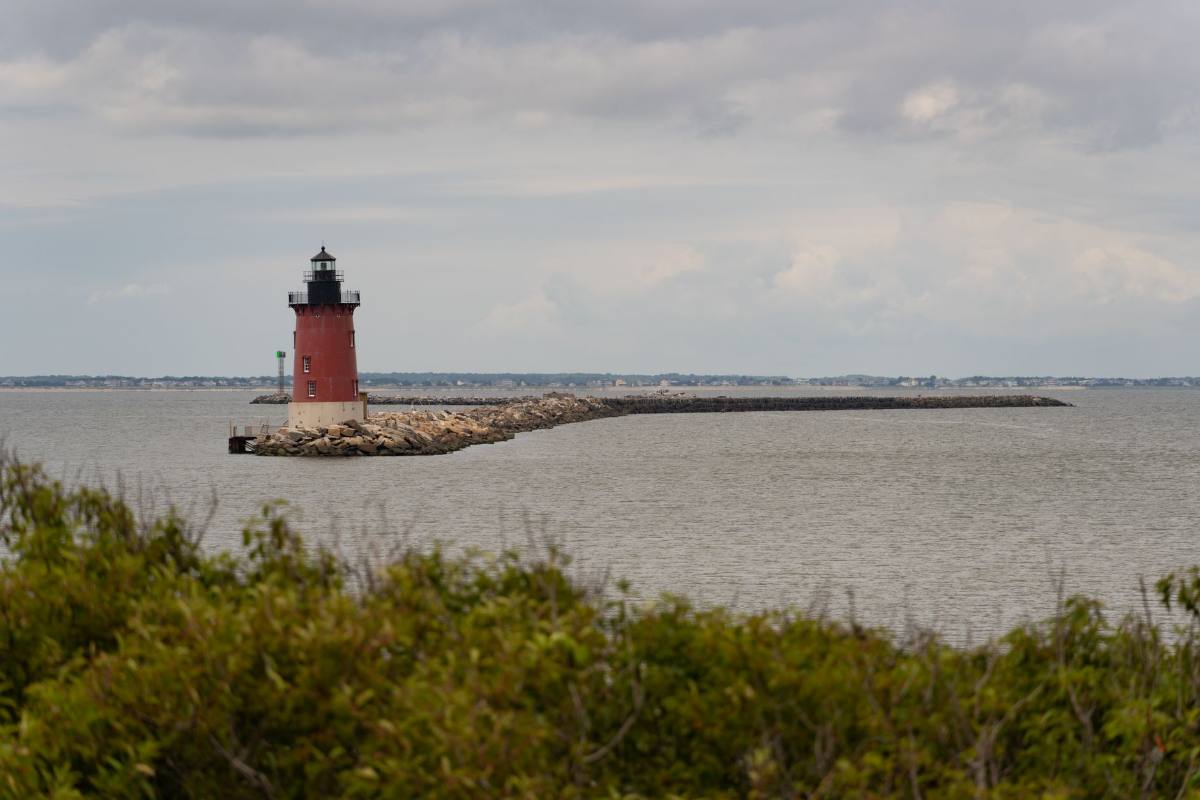 A red and white lighthouse at the end of a long stone breakwater under gray cloud
