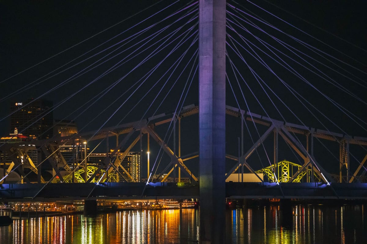 A lit cable-stayed bridge over a river at night with a city glowing behind it