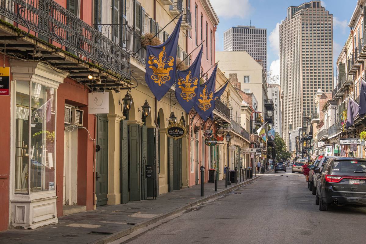 A narrow street of balconied townhouses with flags out, towers rising behind