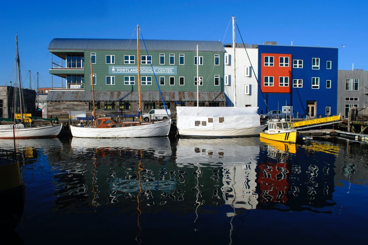 Boats moored along a working waterfront in front of low brick and timber buildings