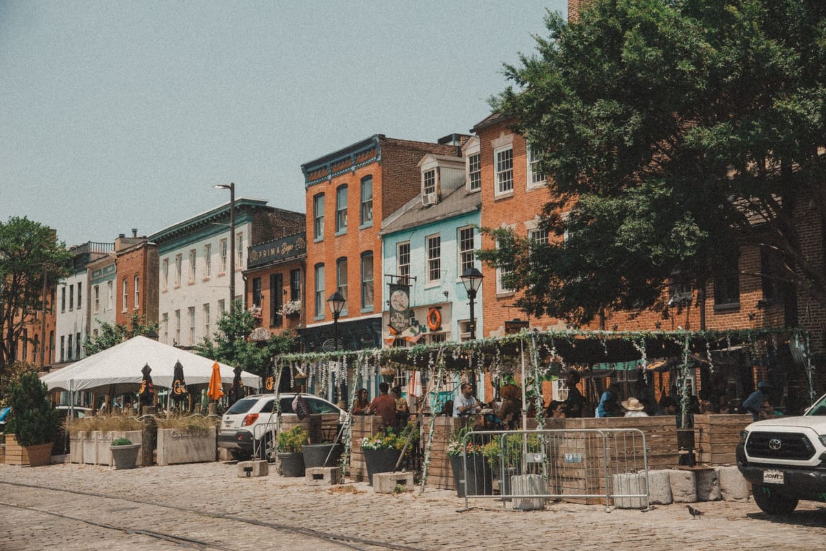 A street of colorful row houses with cafe awnings and tables on a summer afternoon