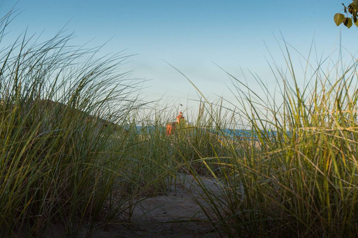 A red lighthouse seen through dune grass across a channel