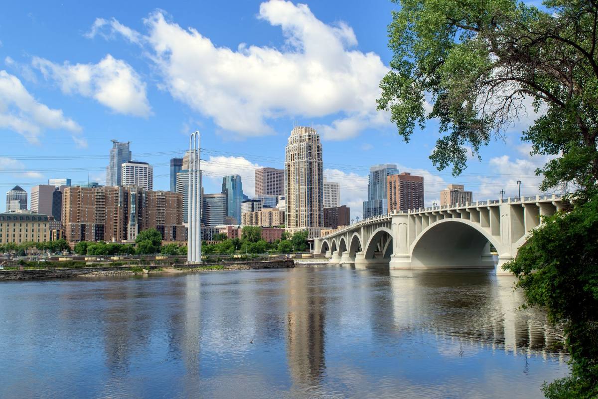 A stone arch bridge crossing a broad river below a downtown skyline