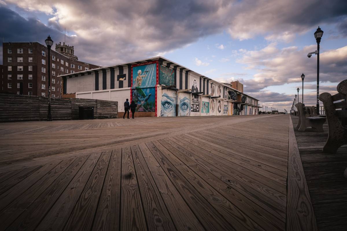 An empty timber boardwalk beside a mural-painted pavilion under a dramatic sky