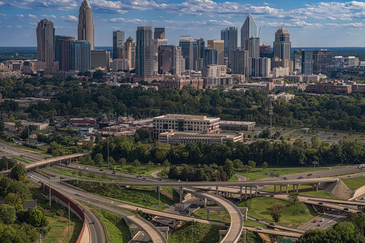 A cluster of glass towers above a green city, highways curving in the foreground