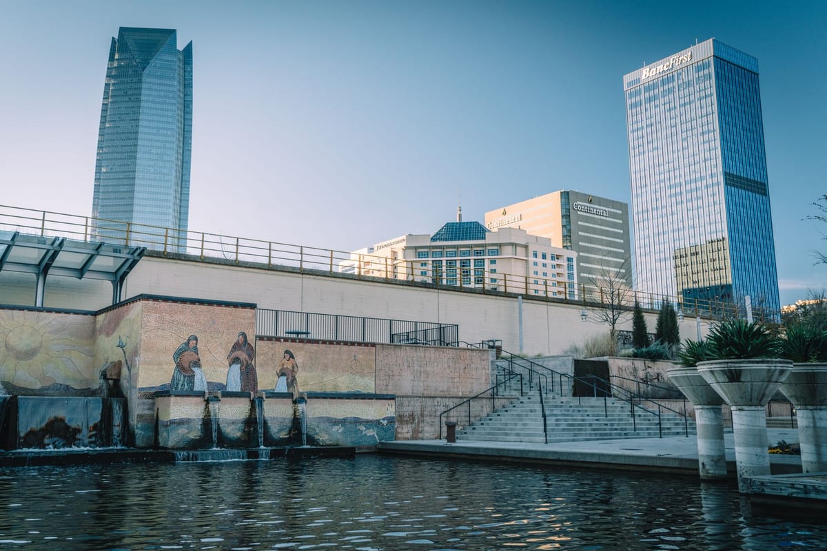 Glass office towers above a canal wall set with a tiled mural and stepped waterfront