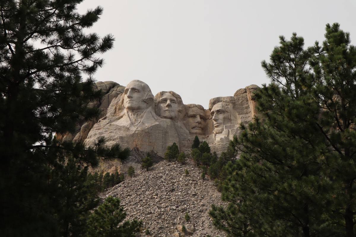 Four presidential faces carved into a granite mountain above pine trees