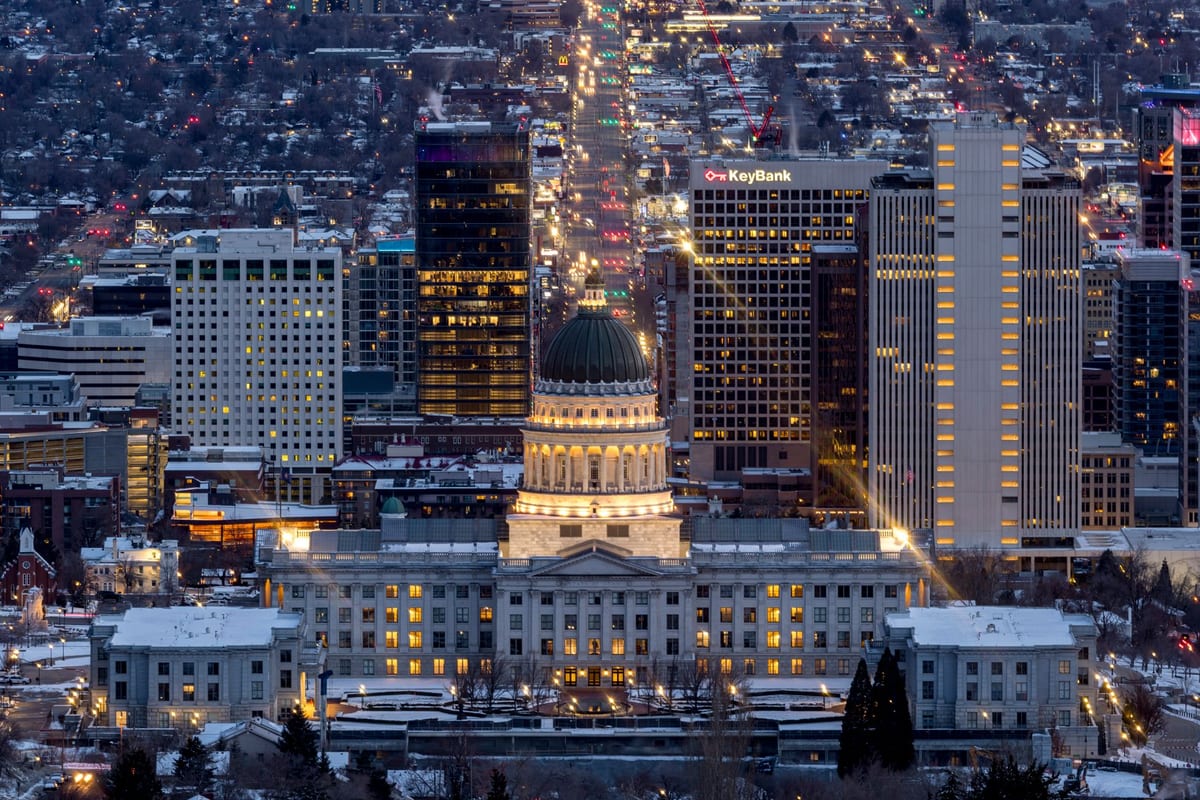 A lit city grid at night below a domed capitol on a rise